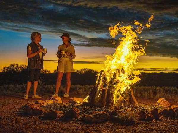 Two guests beside a bush campfire at dusk