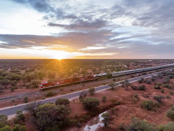 The Ghan running beside a red road as the sun rises over the outback