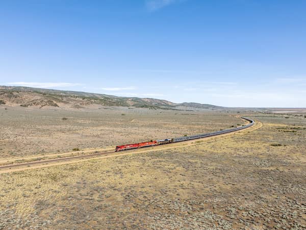 The Ghan's red locomotive winding across open plain beneath a blue sky