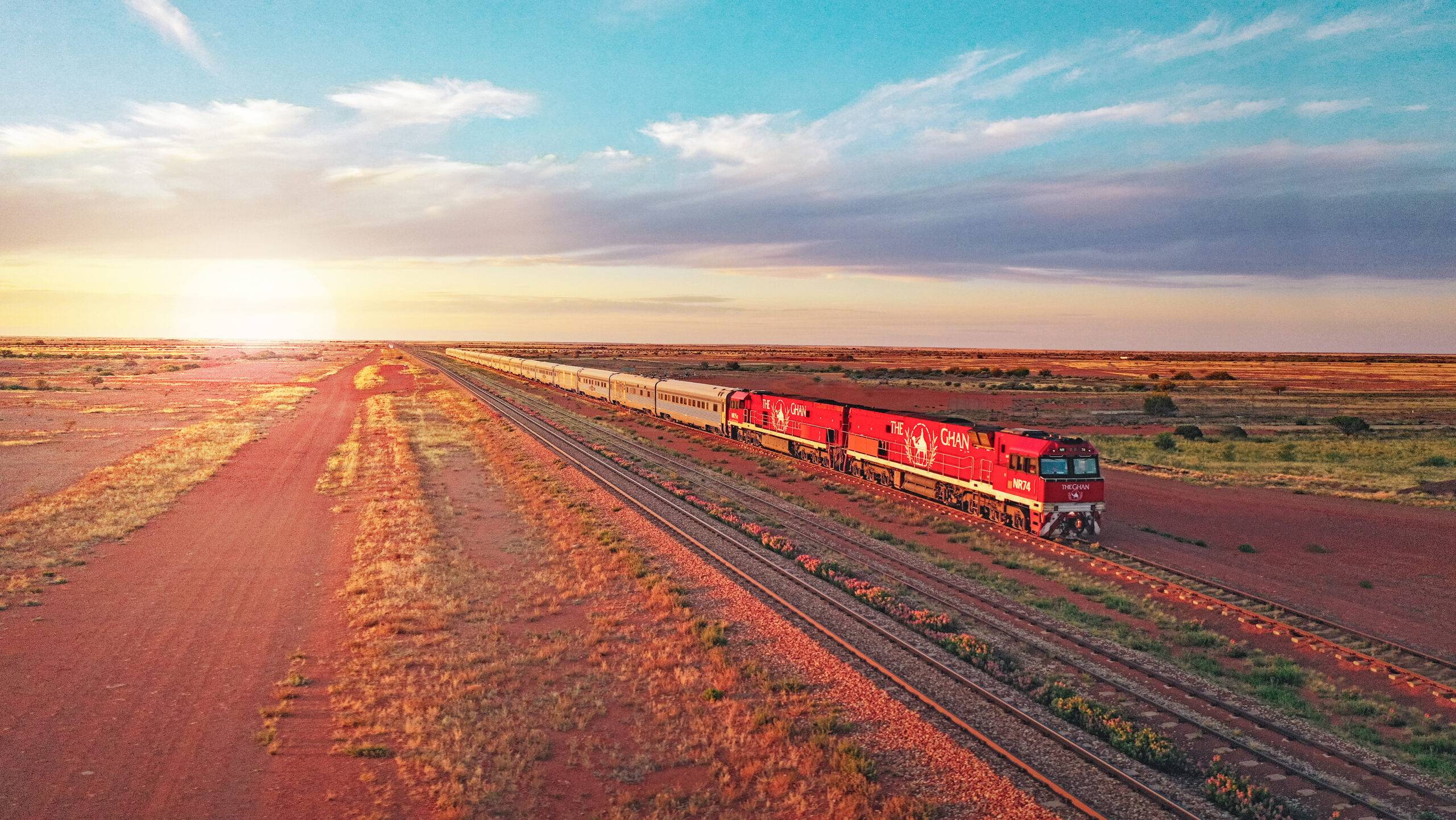 The Ghan's red locomotive and silver carriages travelling through the Australian outback